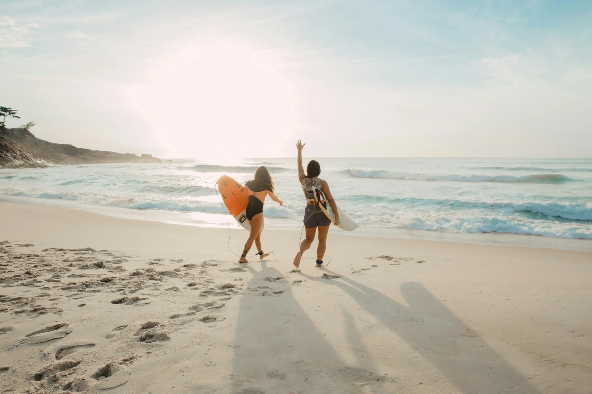Two female surfer on the beach, going towards the sea.