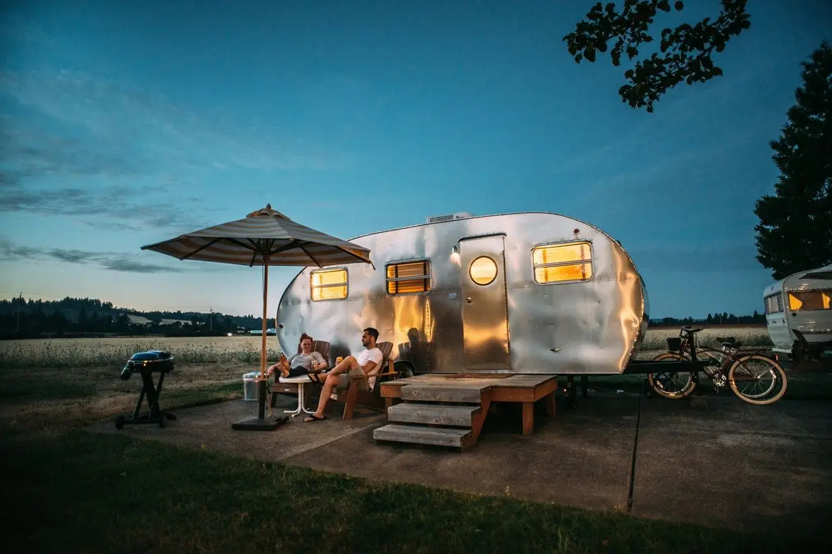 A man and a woman sitting in front of a RV trailer.