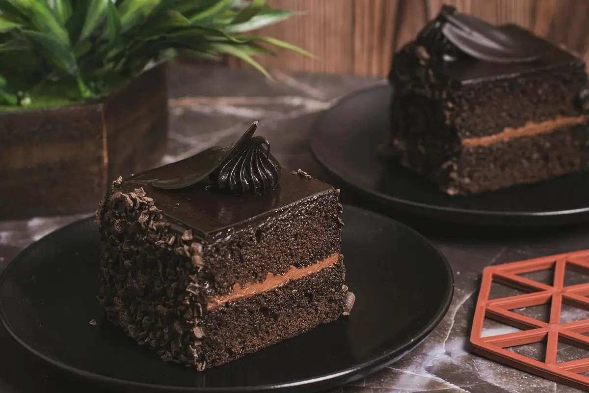 Two slices of dark chocolate cake on dark brown plate on a table.