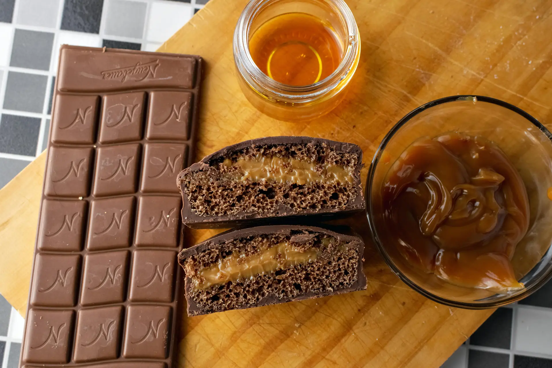 Chocolate bar, chocolate filled with caramel, caramel in a bowl and honey kept on a wooden surface.