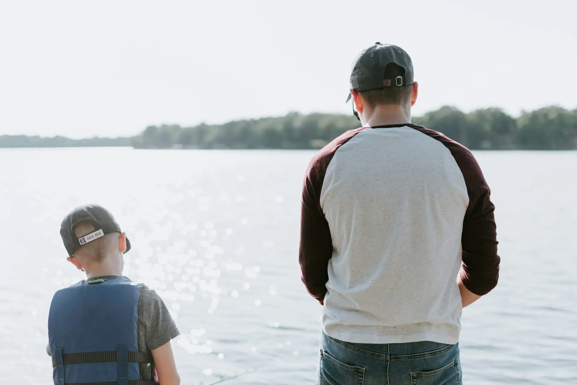 A man and a kid standing front of a large body of water, probably a lake.