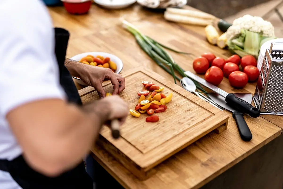 A chef cutting vegetables on a cutting board which is placed on a wooden table.