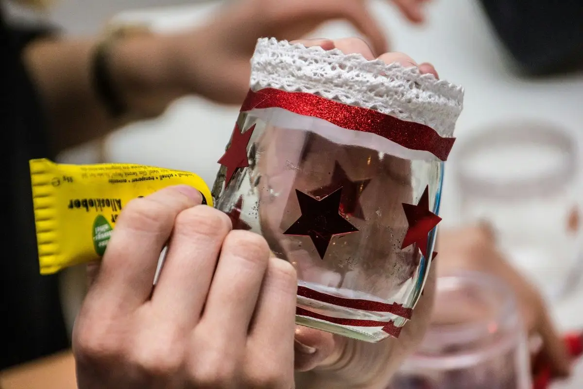 A person decorating a glass piece with glue and laces.