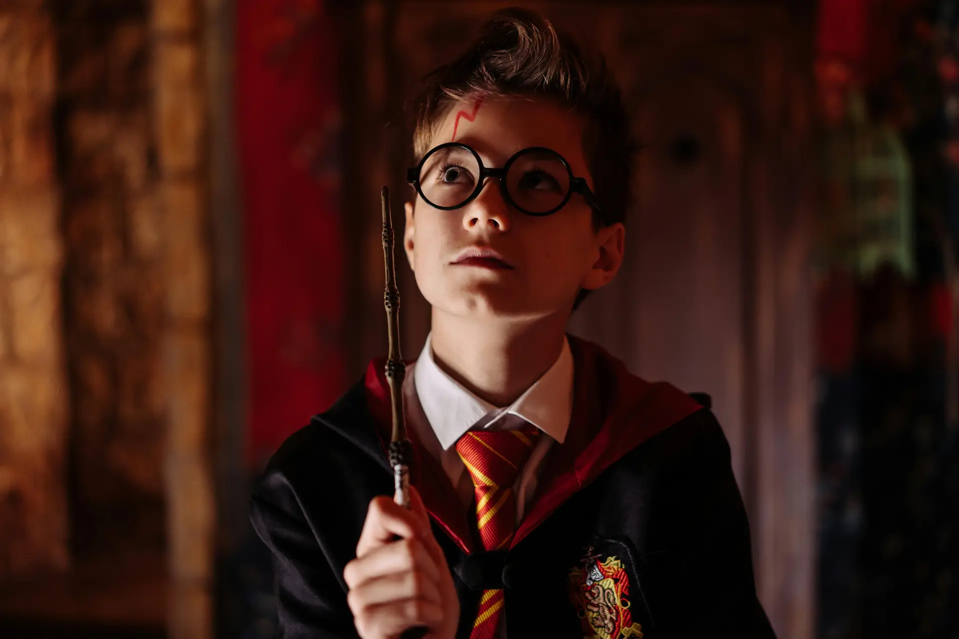 A child cosplaying as harry potter. He has a wand in hand.