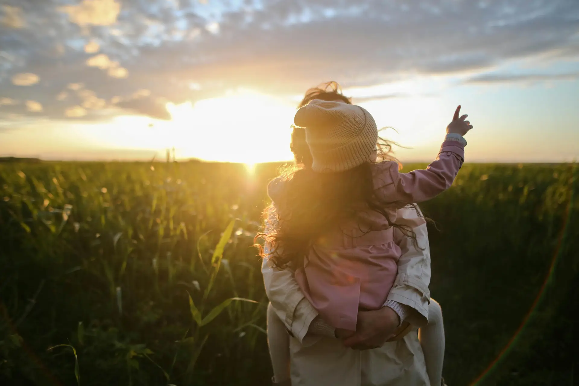 A photo of a mother holding a baby in her arms while the sun is setting in the background.
