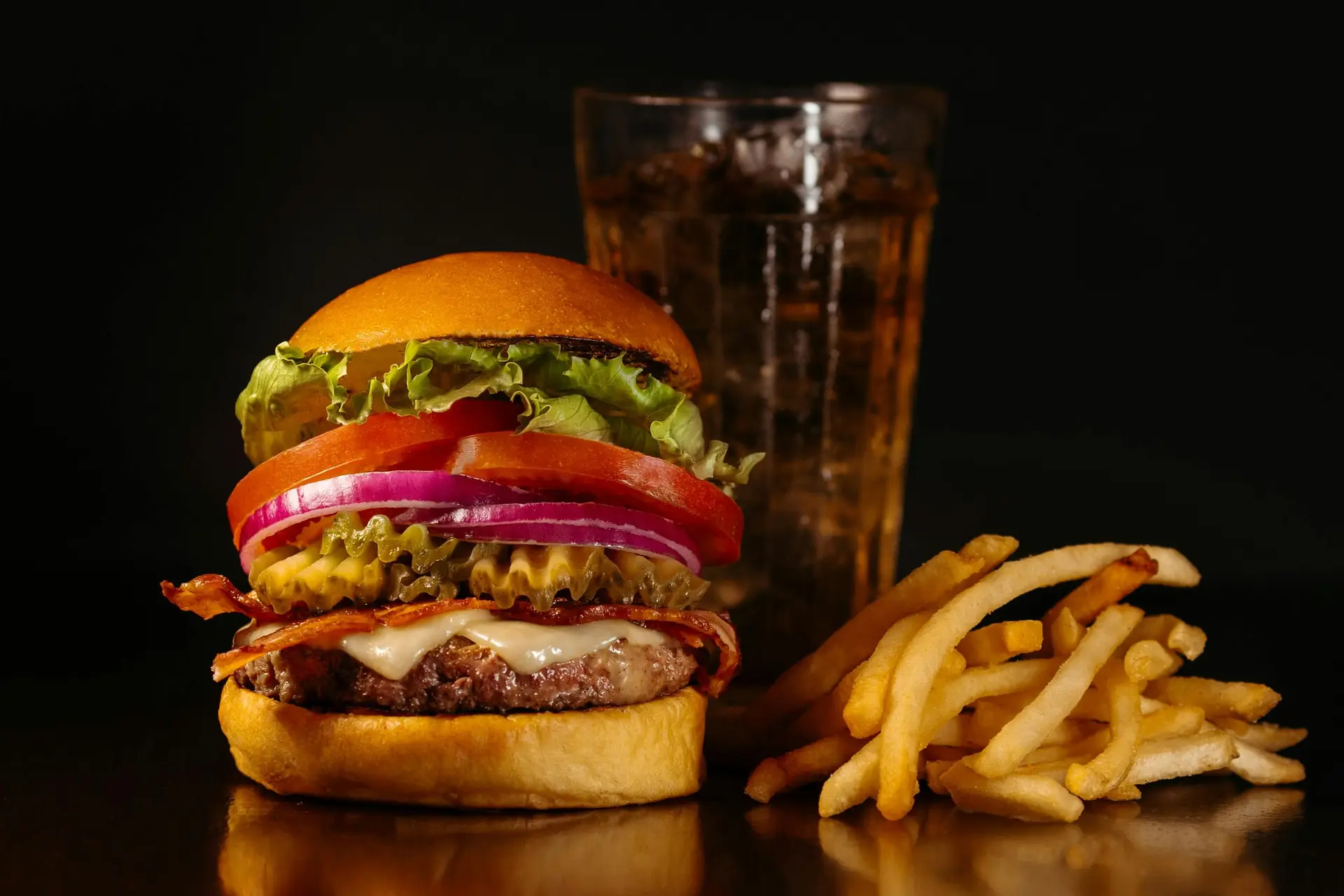 Juicy burger on a glassy surface along with french fries and drink.