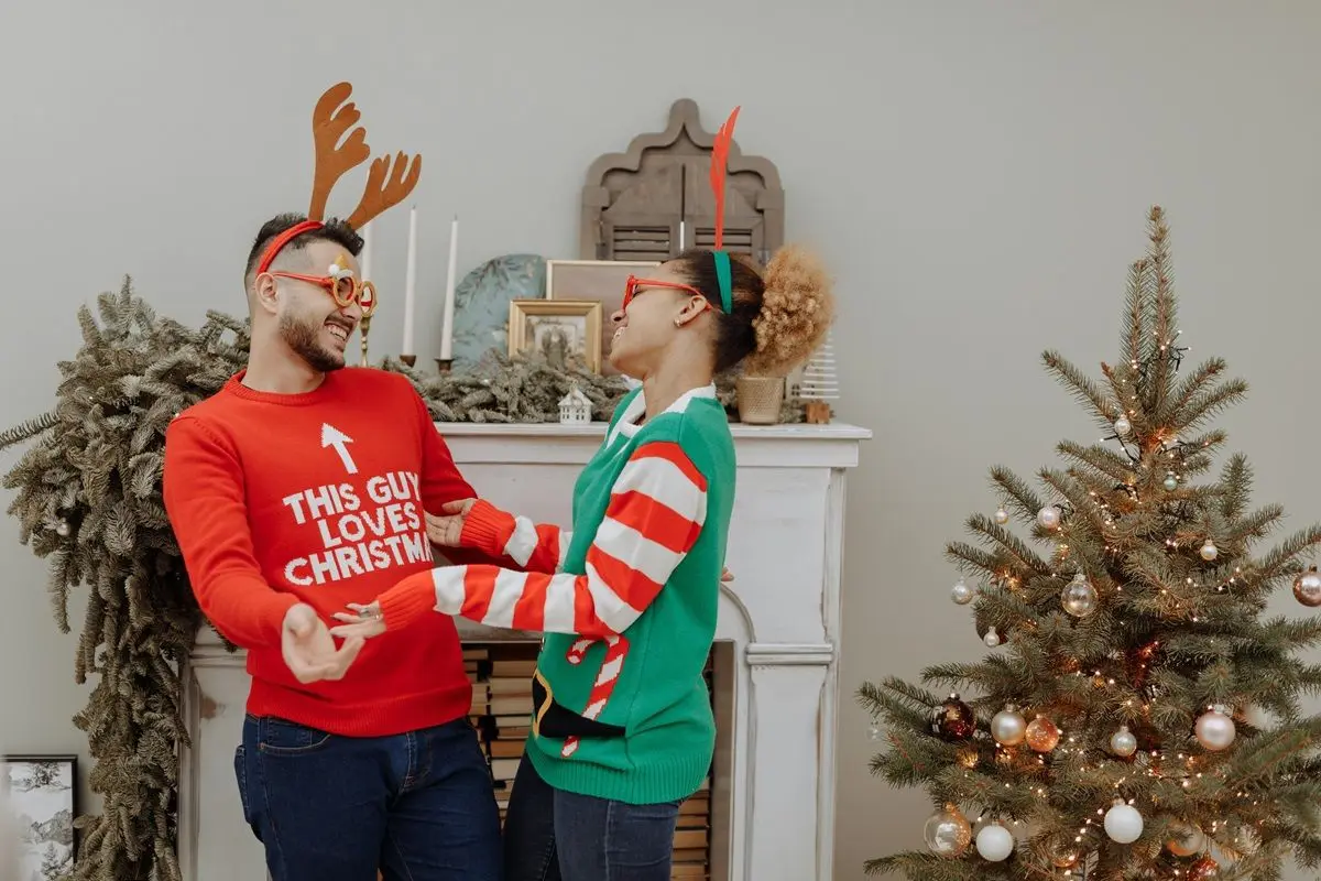 A person wearing a red sweater with the text This Person Loves Christmas on it while another person wearing a green sweater.