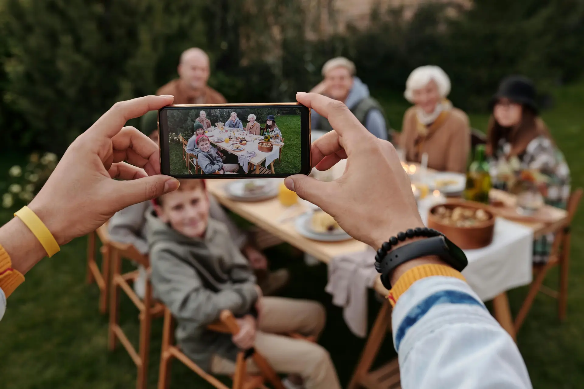A person taking photo of a family eating outside in the yard.