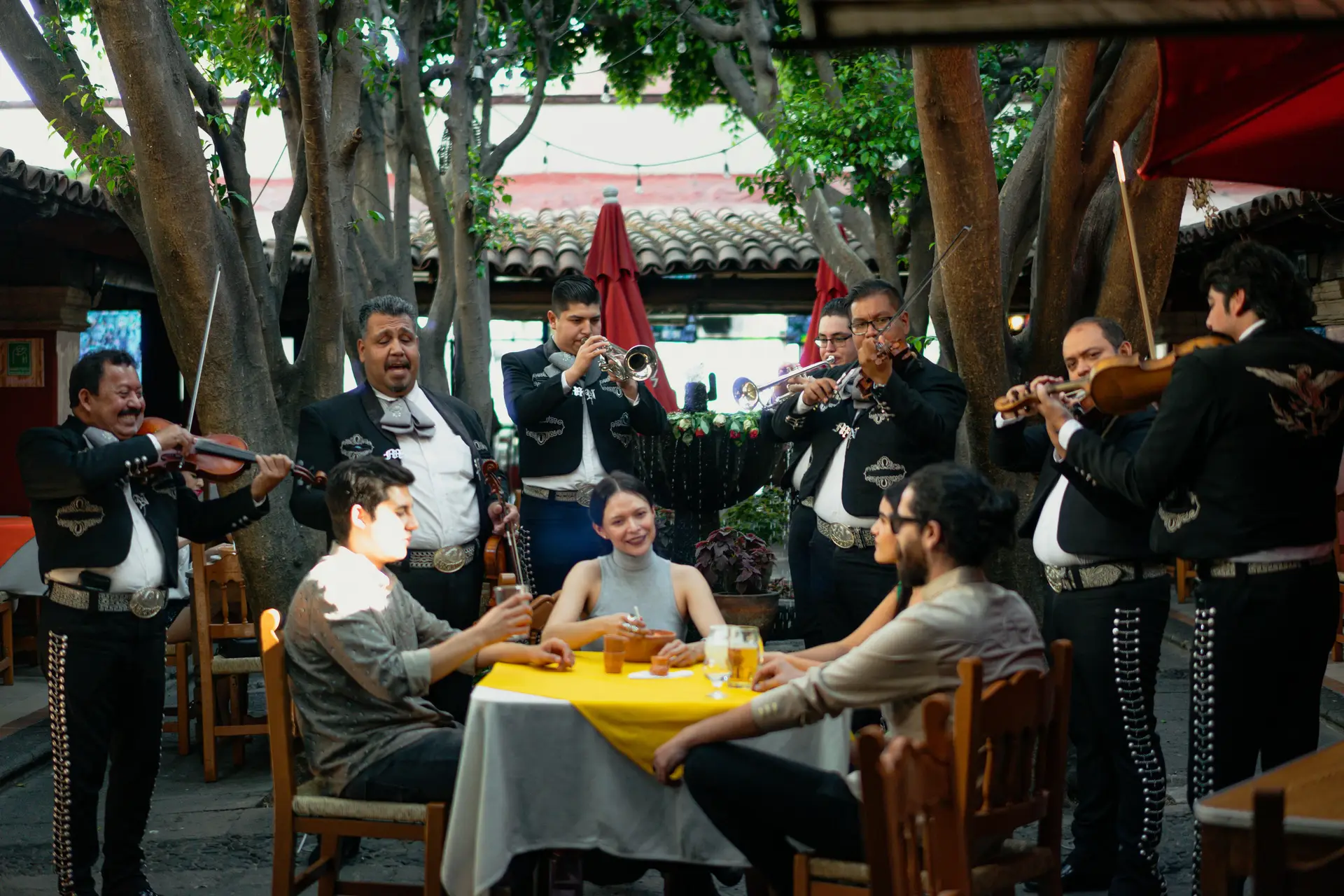 A group of people listening to a mariachi band while eating food.