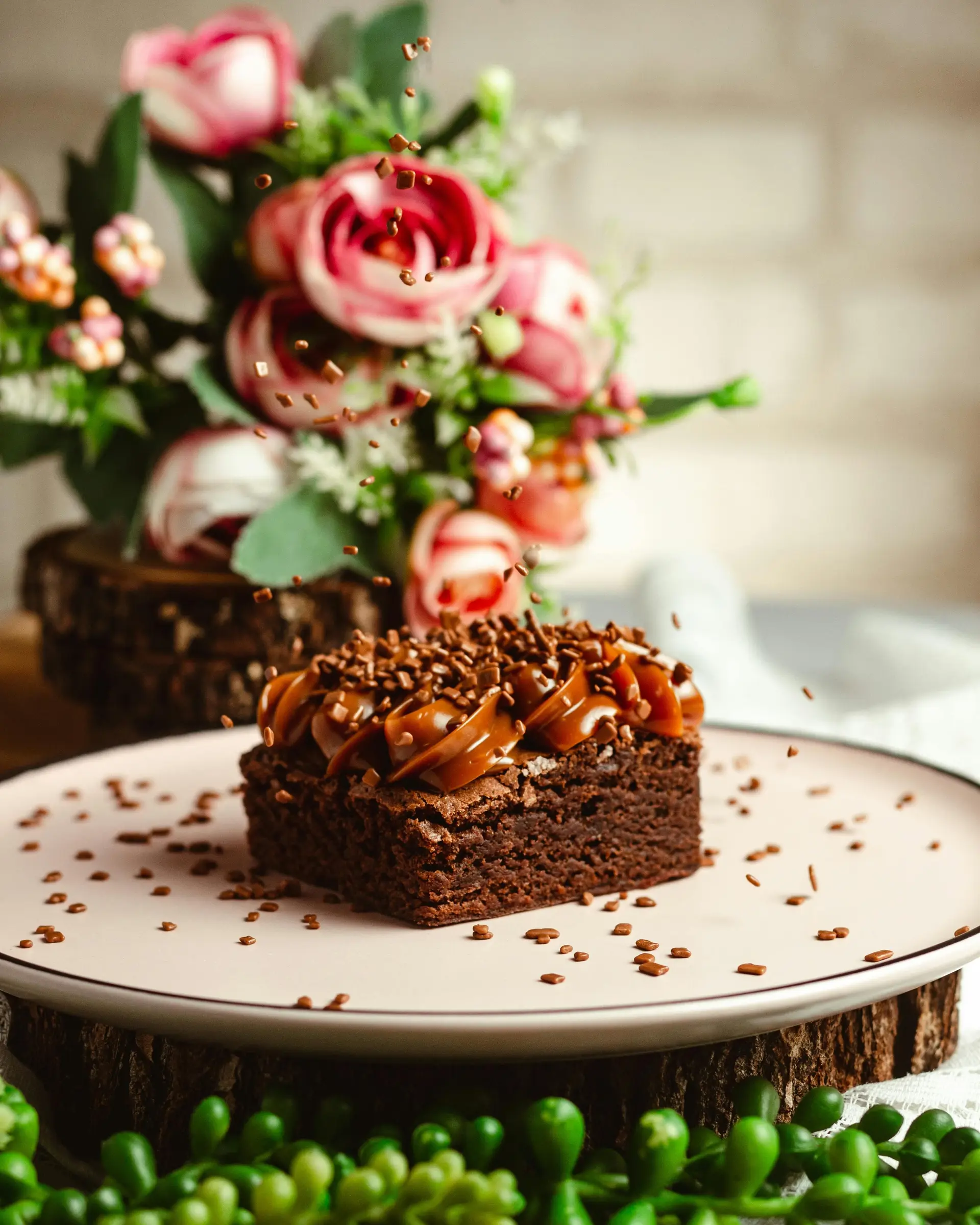 Chocolate brownie topped with caramel, presented on a circular plate with chocolate shavings.