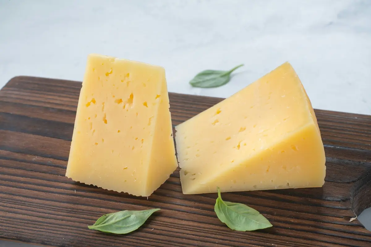 Two pieces of cheese on a wooden board along with some leaves.