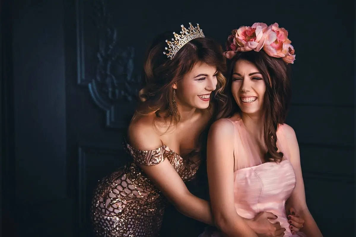 Two person wearing princess dress, one with a tiara on her head and the other with a flower tiara on her head.