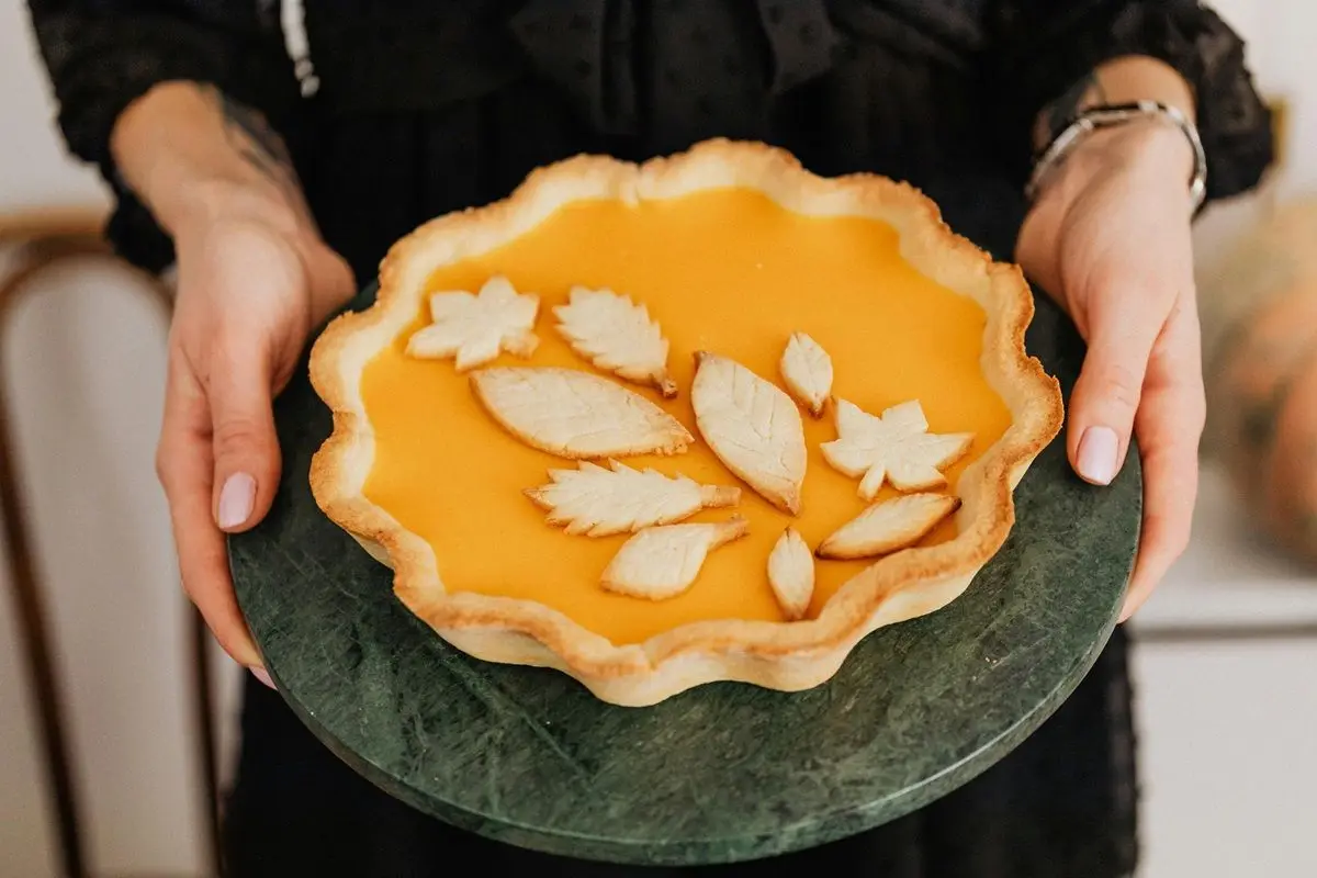 A person holding a decorated pumpkin pie.