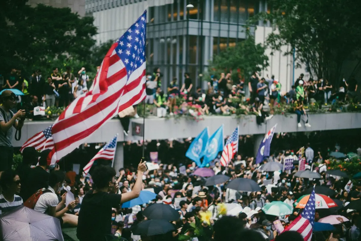 A crowd of people holding american flags and umbrellas.