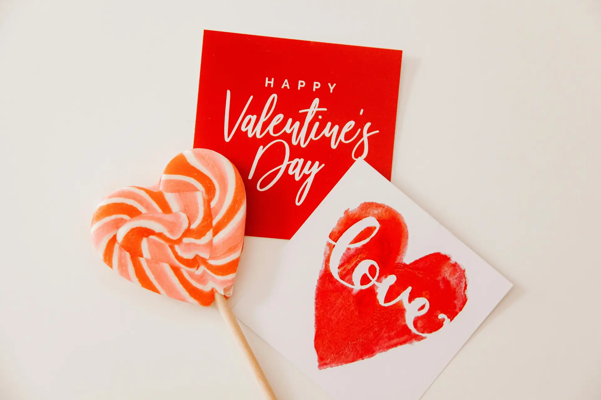 Valentine's day cards and a heart shaped lollipop kept on a white surface.