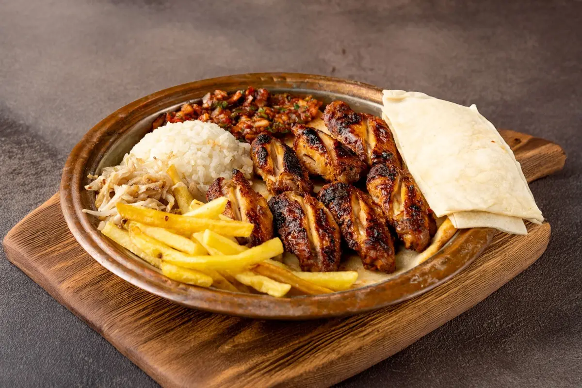 Grilled chicken wings with rice, fries, and tortillas on a wooden platter.