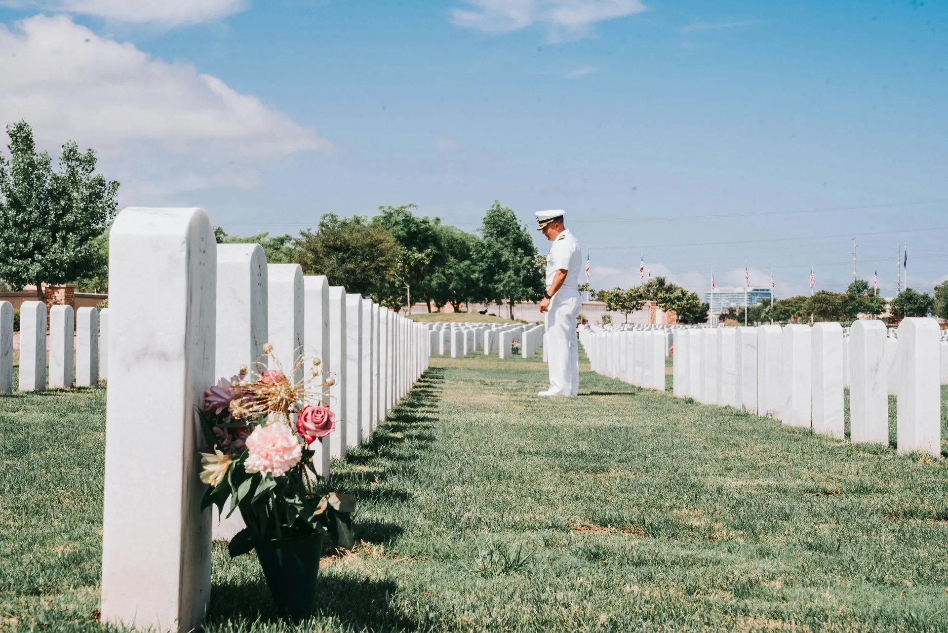 A man paying respect on the grave of a fallen soldier. There's a boquet of flower near one gravestone.
