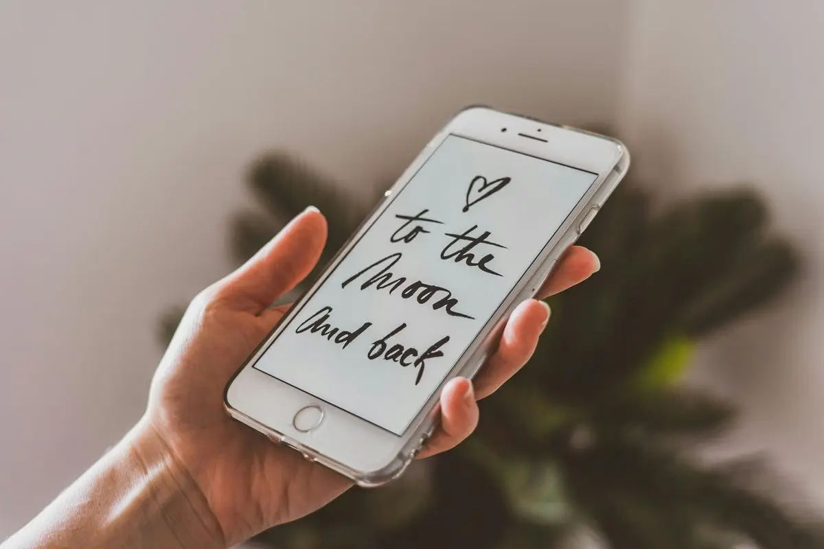 A person holding a silver iPhone that has the e-greetings love ou to the moon and back.