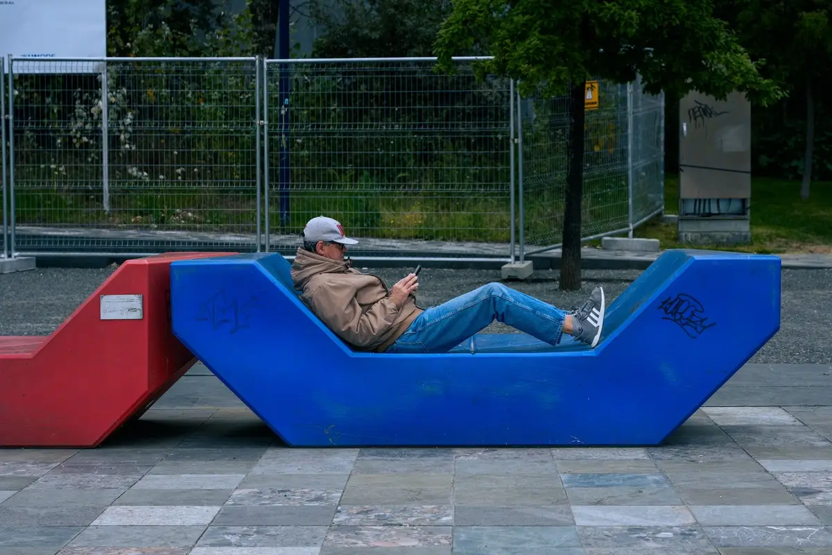 Man relaxing on a colorful bench outdoors in Tirana, Albania, urban lifestyle scene.