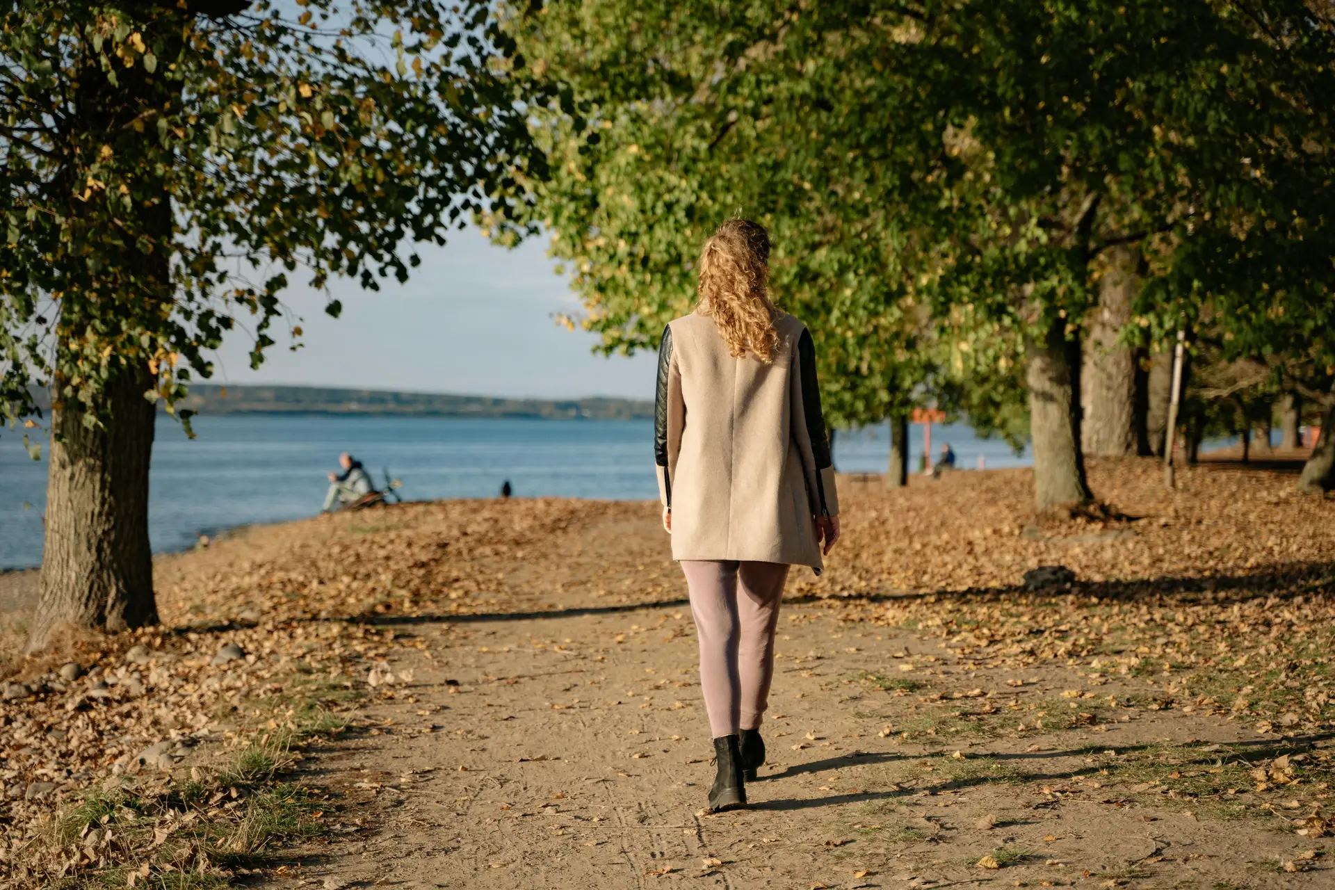 A woman walking in a park situated near a lake.
