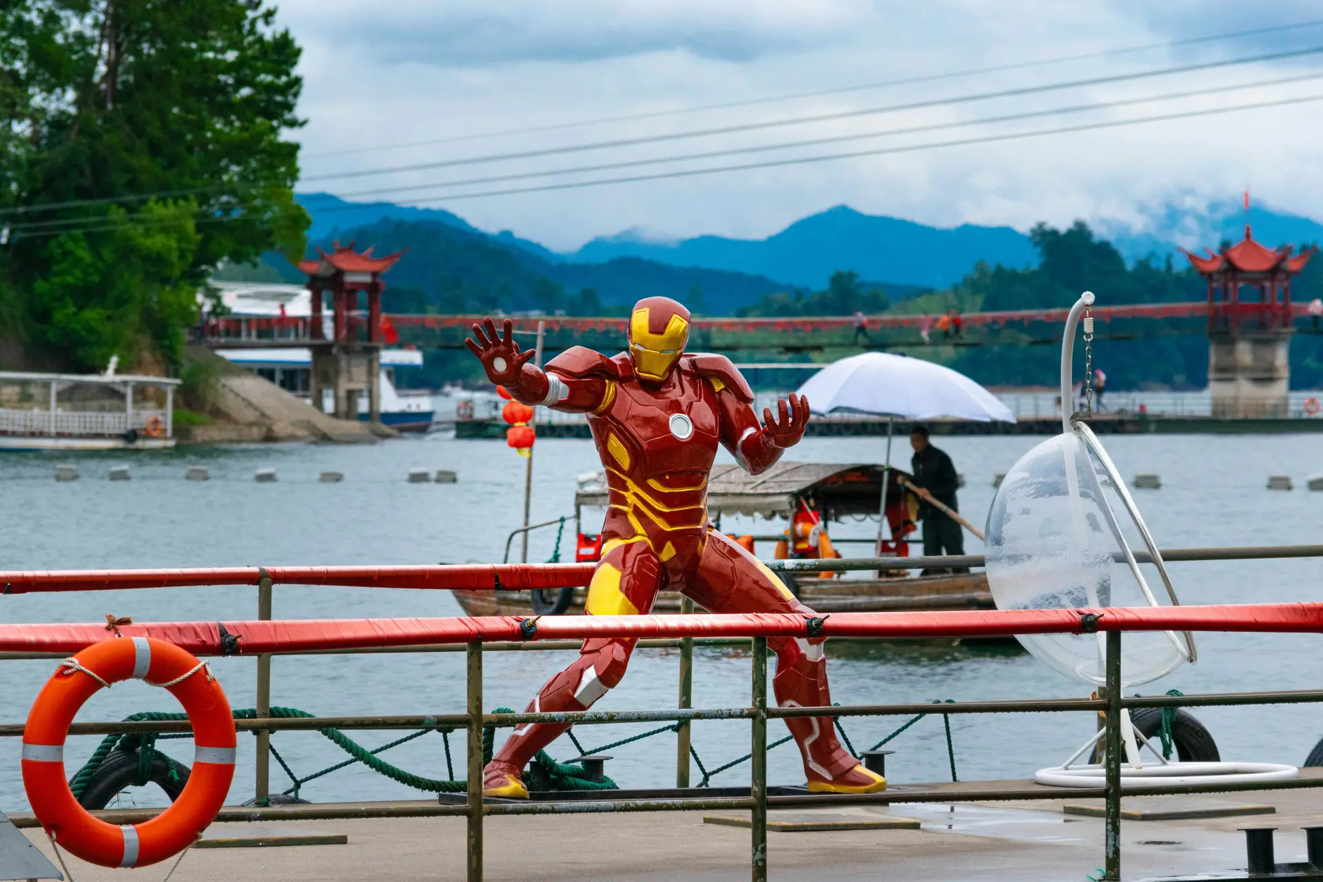 On a dock near a river a statue of iron man is seen prepped up.