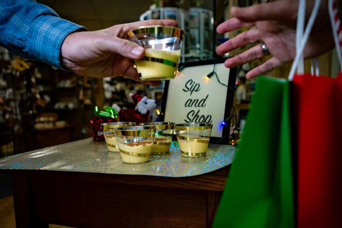 A person handing a glass of eggnog to another person in a shop.