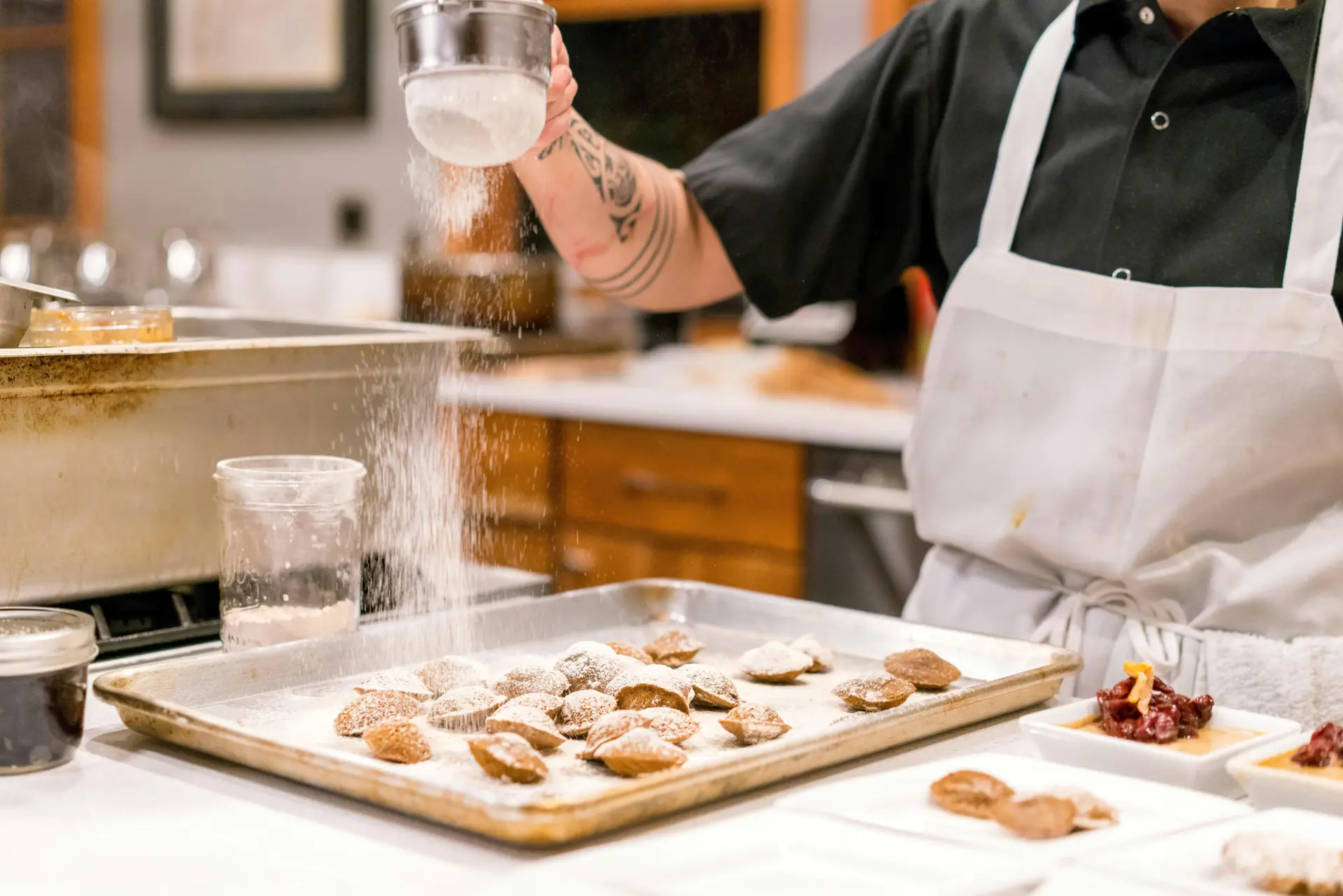 A baker putting powdered sugar on baked goodies.