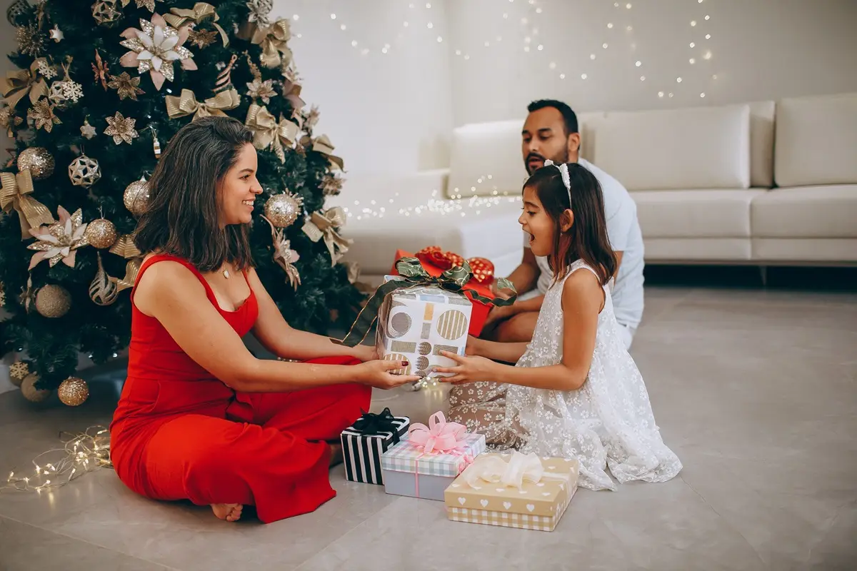 A family enjoys exchanging gifts near a beautifully decorated Christmas tree indoors.