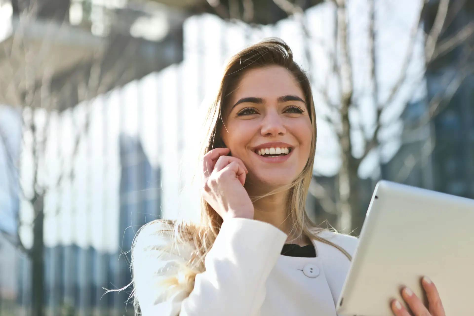 A woman on the phone is laughing as she walks outside her office with a laptop.