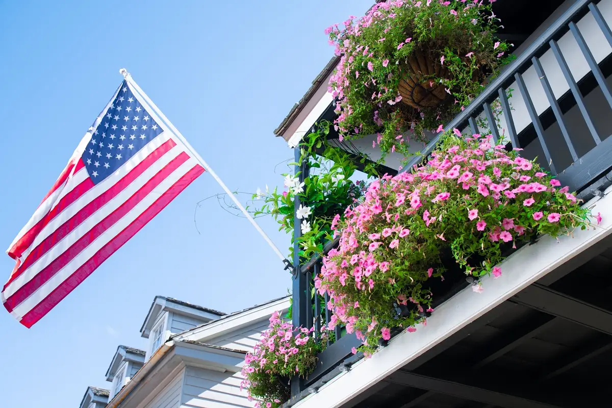 Patriotic display of the American flag with lush pink flowers on a sunny day.