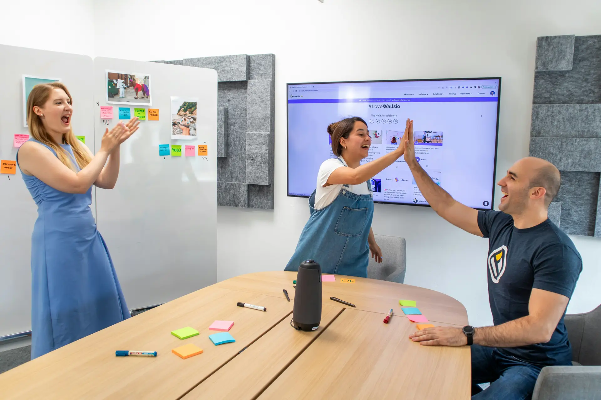 Three office workers in a room, one is sitting down, two standing. One of the worker is highfiving the boss.