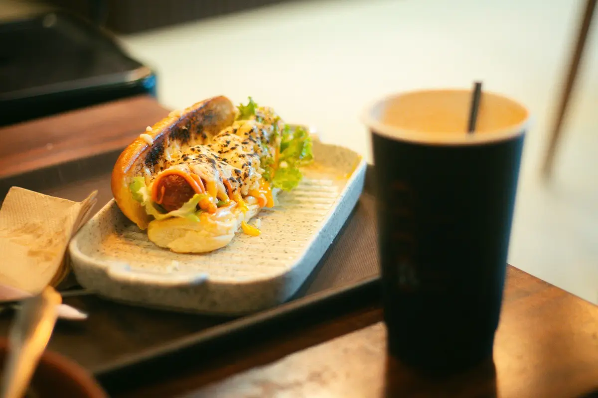 Tasty gourmet hot dog with toppings and drink served on a tray indoors.