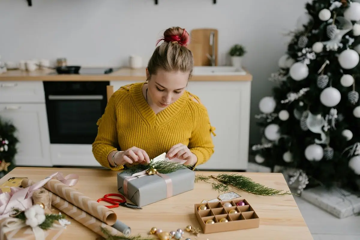 A person wrapping a gift box. A Christmas tree can be seen behind them.