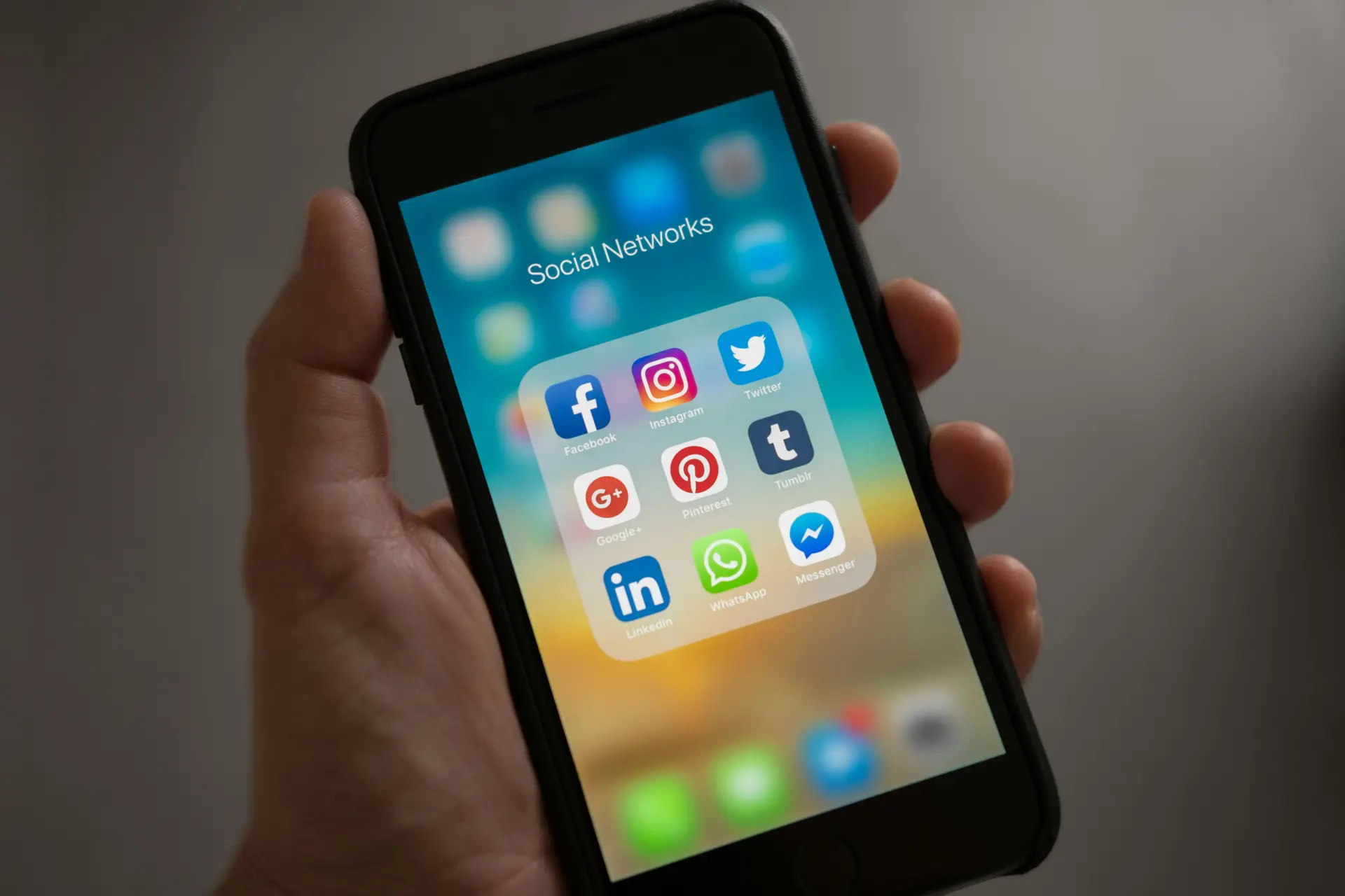 A man holding a phone where a folder full of social media app's icon is shown.