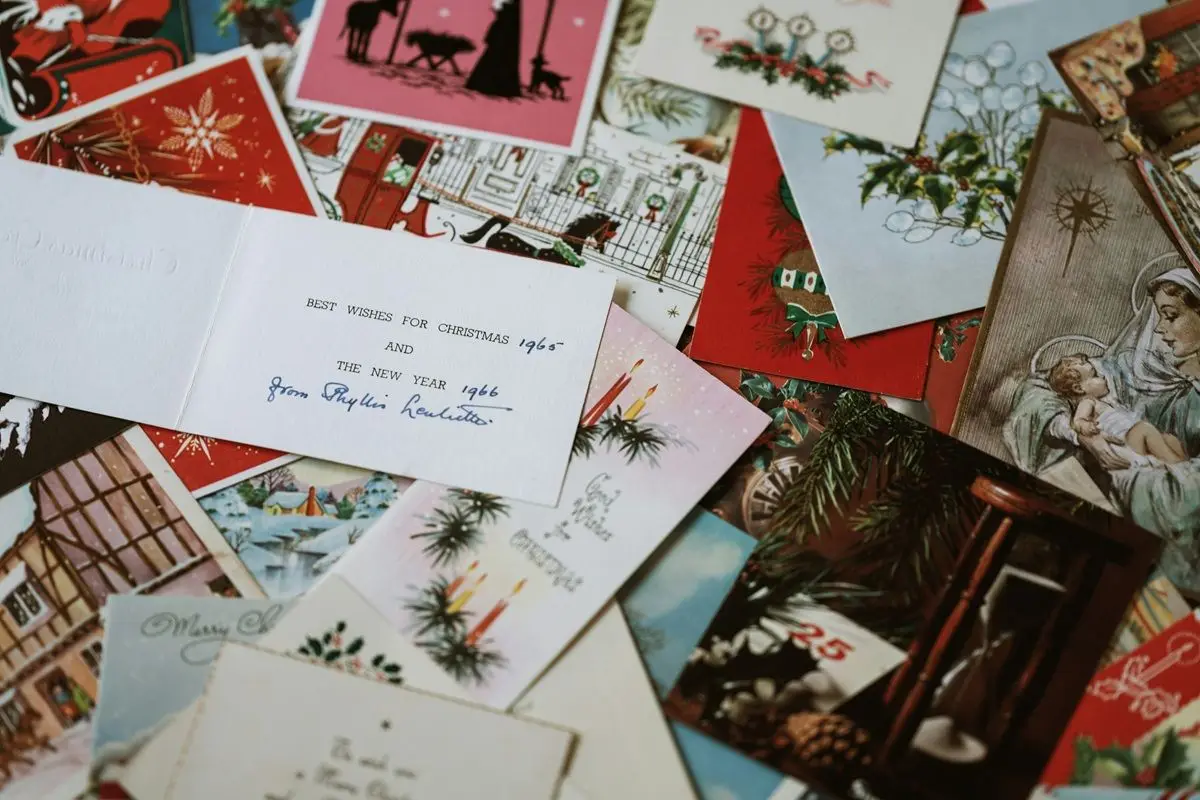 An assortment of Christmas card is laid on a bed and one is open and has the text ' best whishes for Christmas and New year