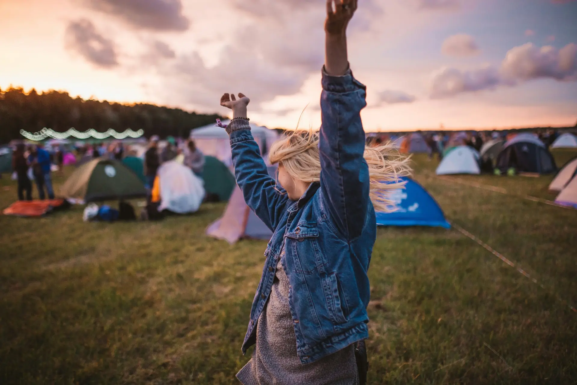 A woman raising her arms in the air in front of tents.