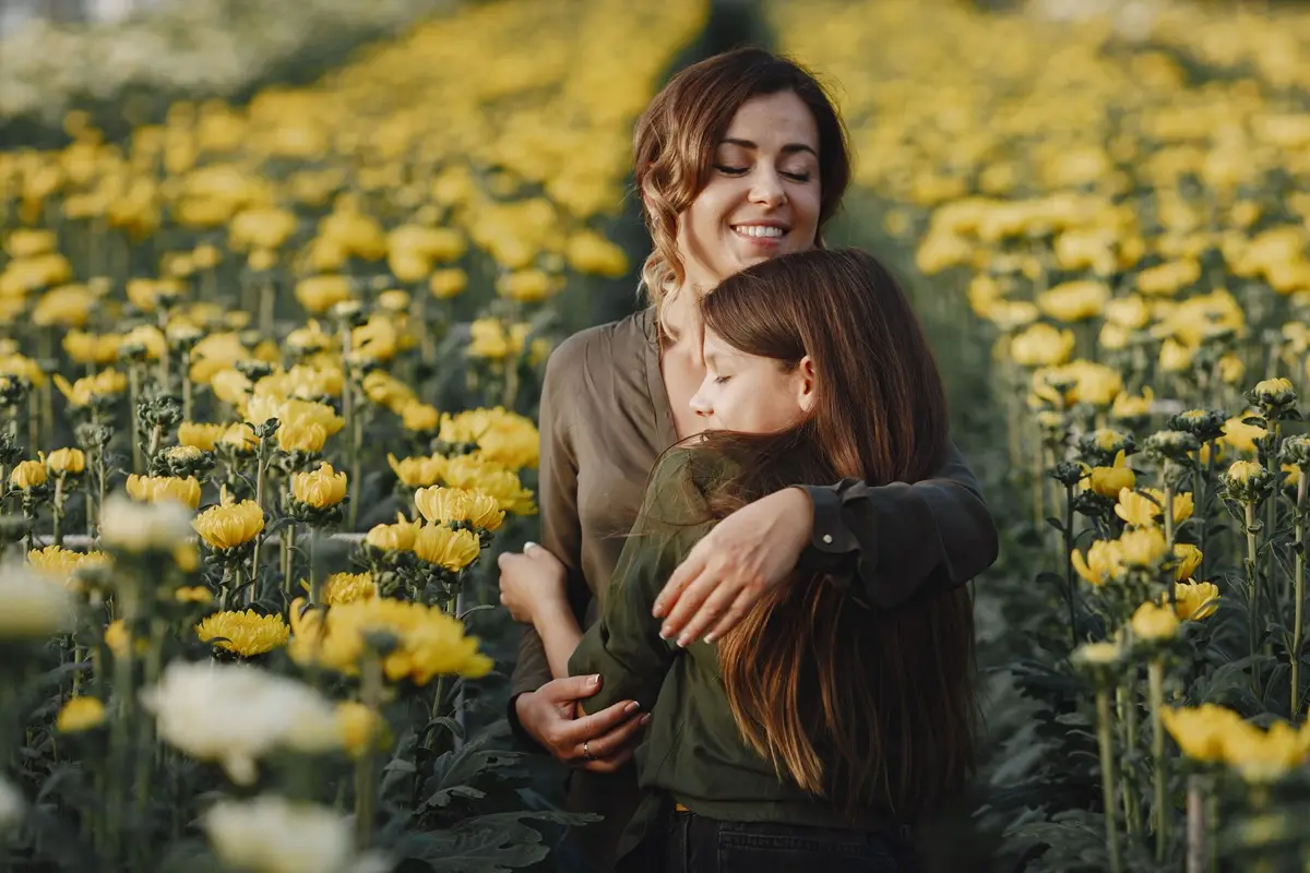 A loving mother and daughter embrace in a field of blooming yellow flowers, conveying warmth and happiness.