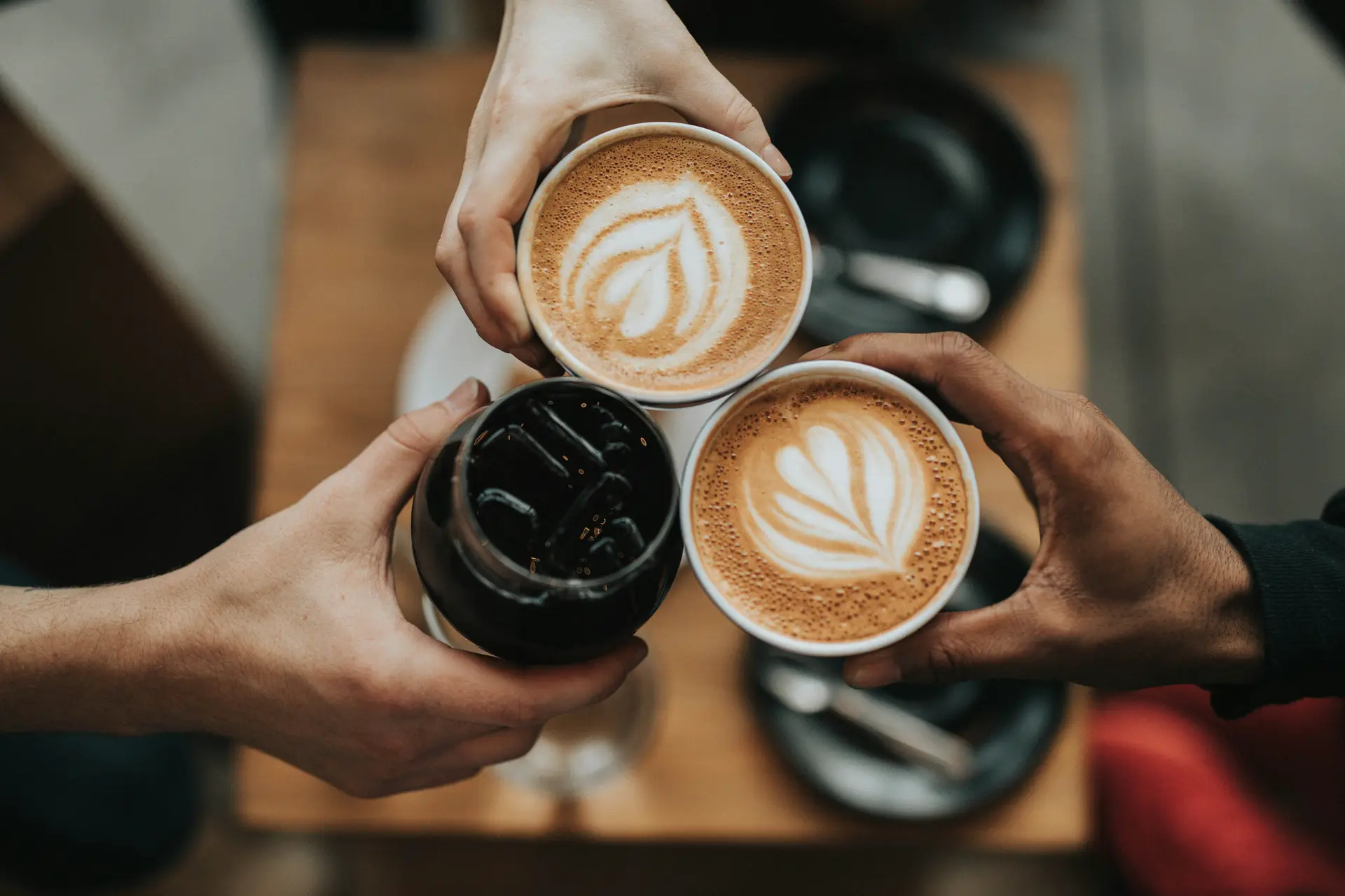 Three person holding beverage cups filled with coffee and soft drinks.
