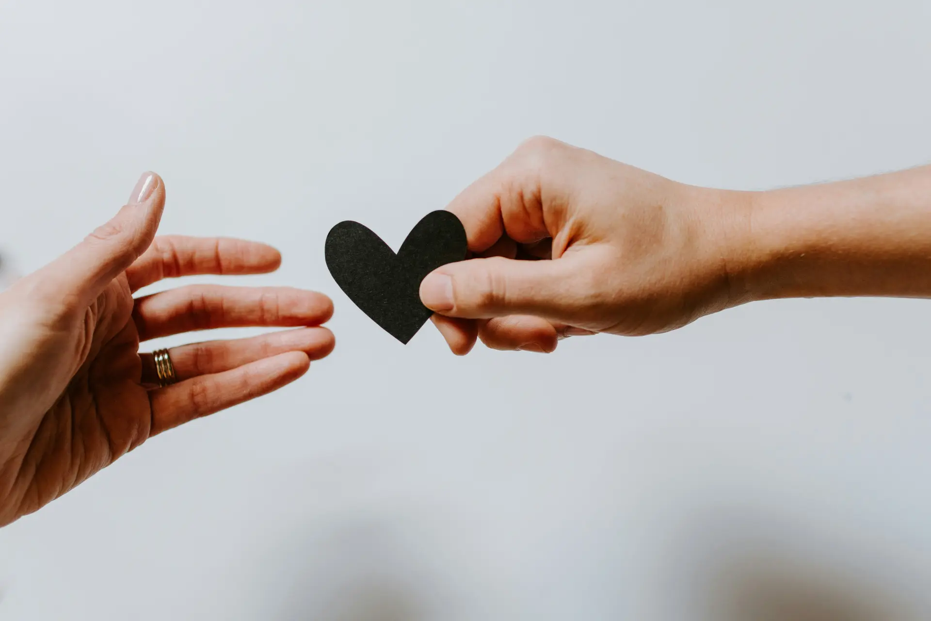 Two hands, one giving another a black shaped heart cutout.