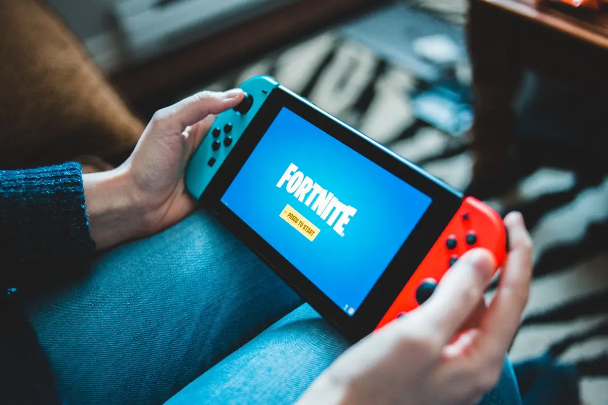 Hands holding a Nintendo Switch with Fortnite game screen indoors.