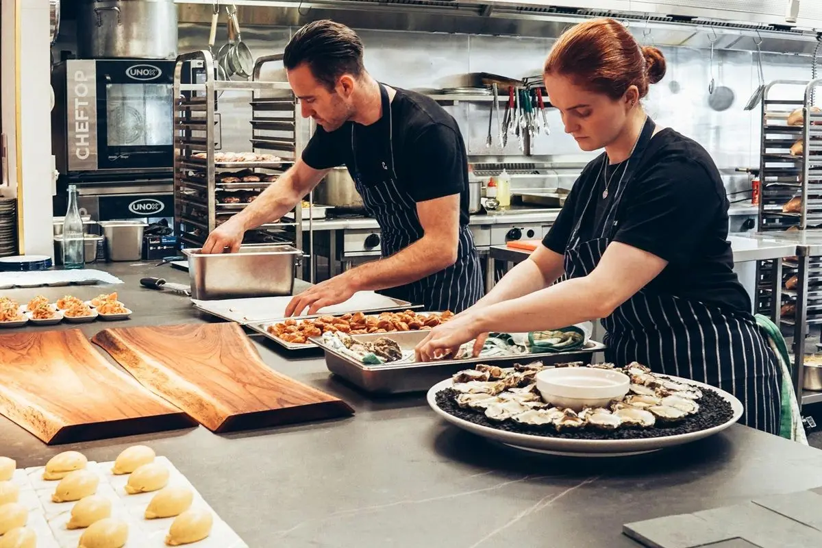 Two chefs wearing black and white striped aprons cooking together.