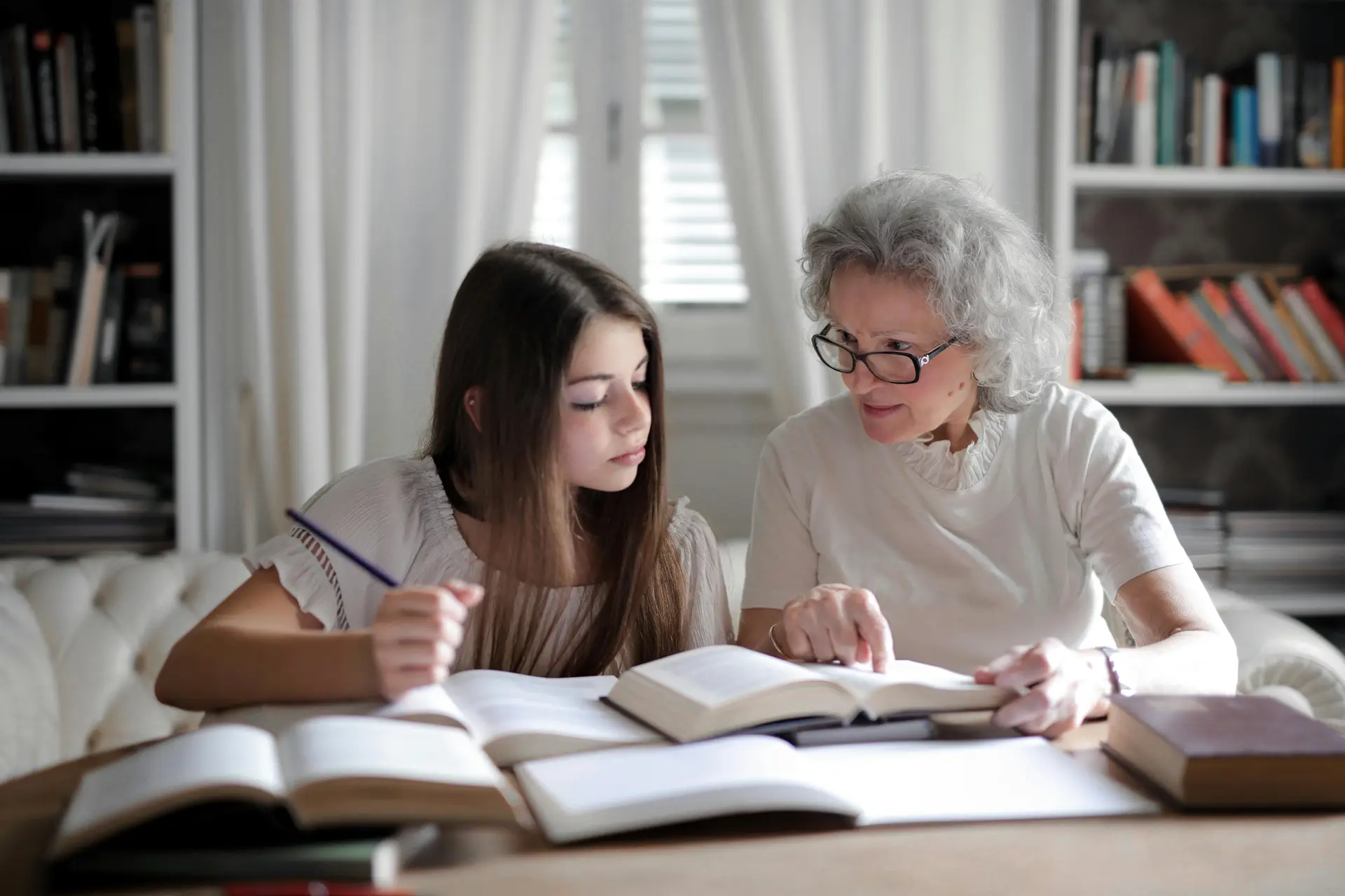 An old female teacher helping a young girl with her studies.