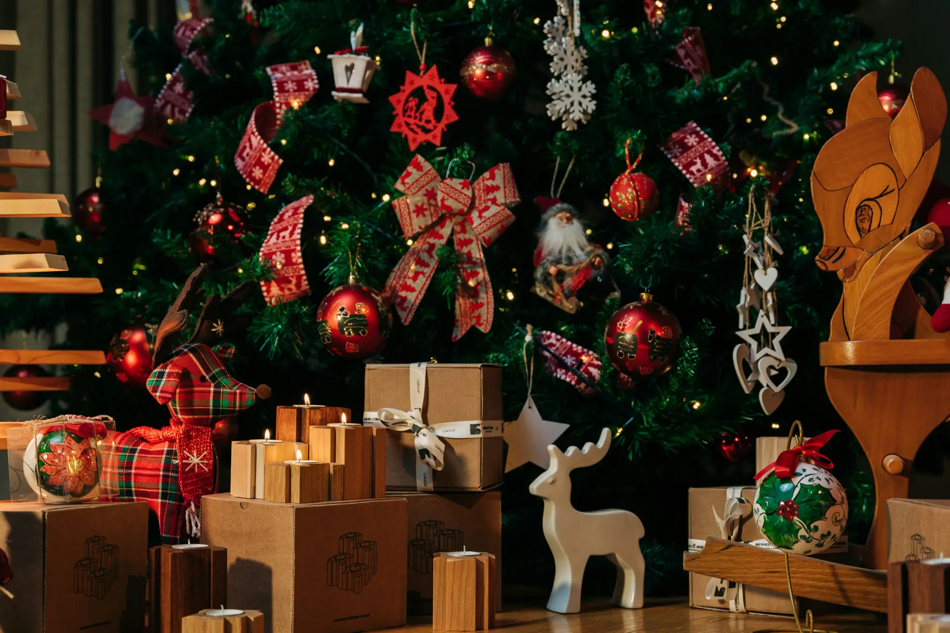 A christmas tree is decorated with various ornaments. Under it there are many giftboxes and statues.