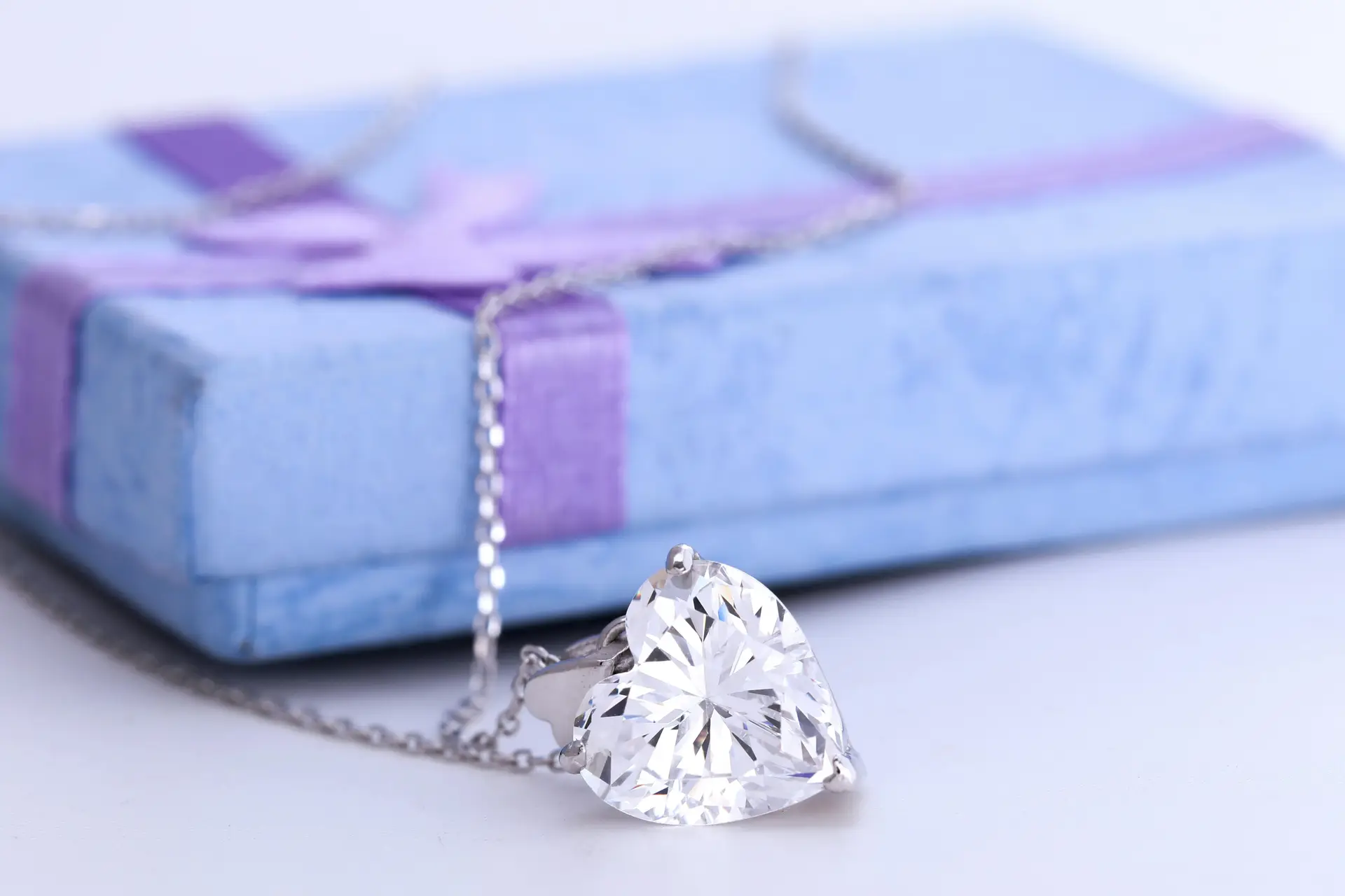 A heart shaped diamong pendant necklace with a giftbox on a glossy surface.