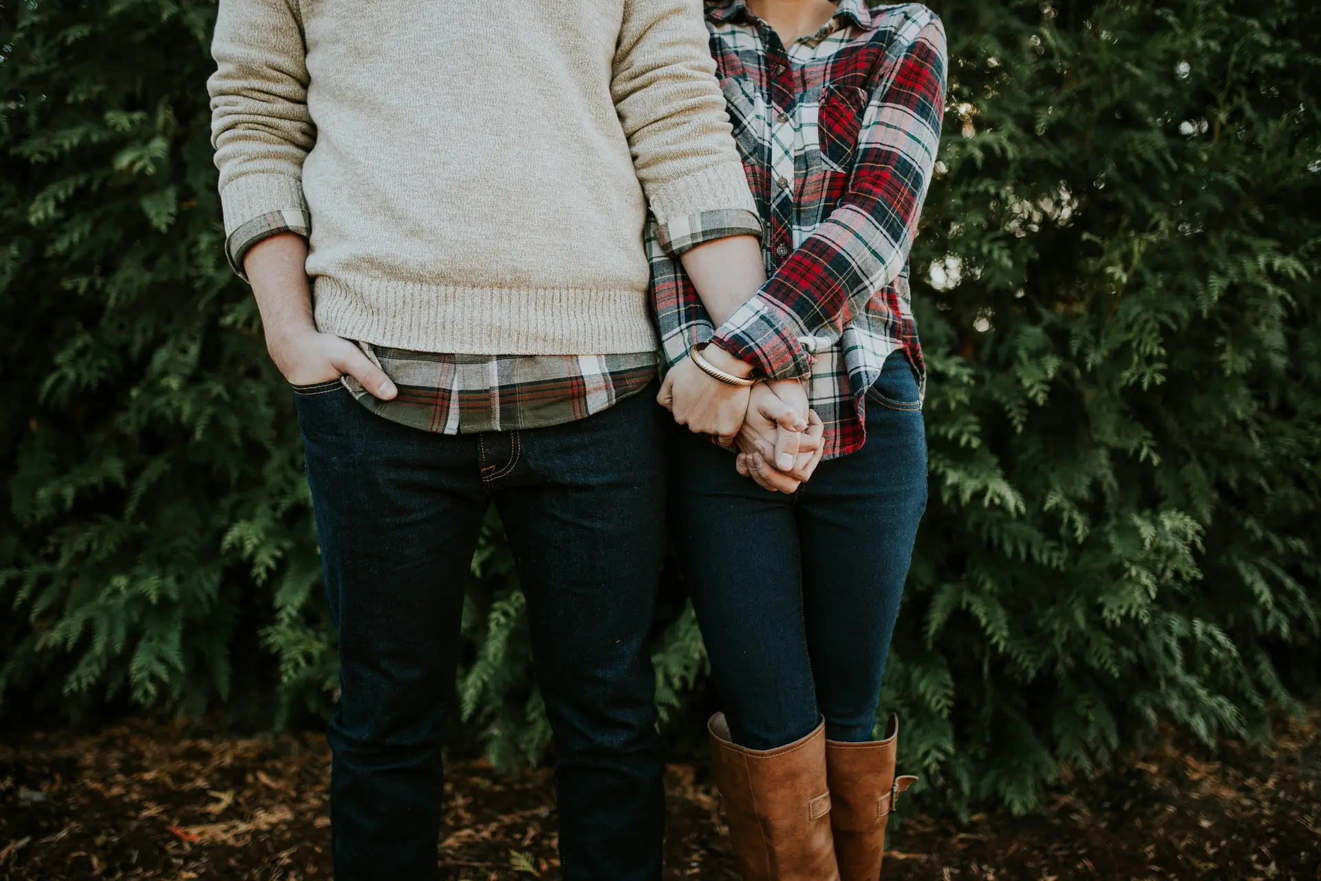 Boyfriend holding hand of his gf. In the background some plants can be seen.