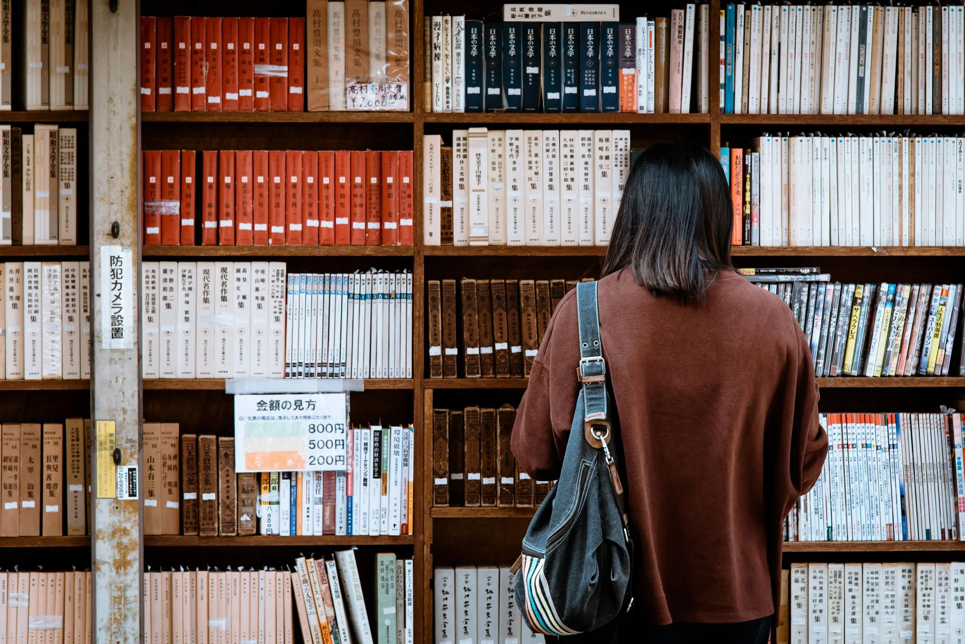 Woman wearing brown shirt carrying black leather bag on front of library books.