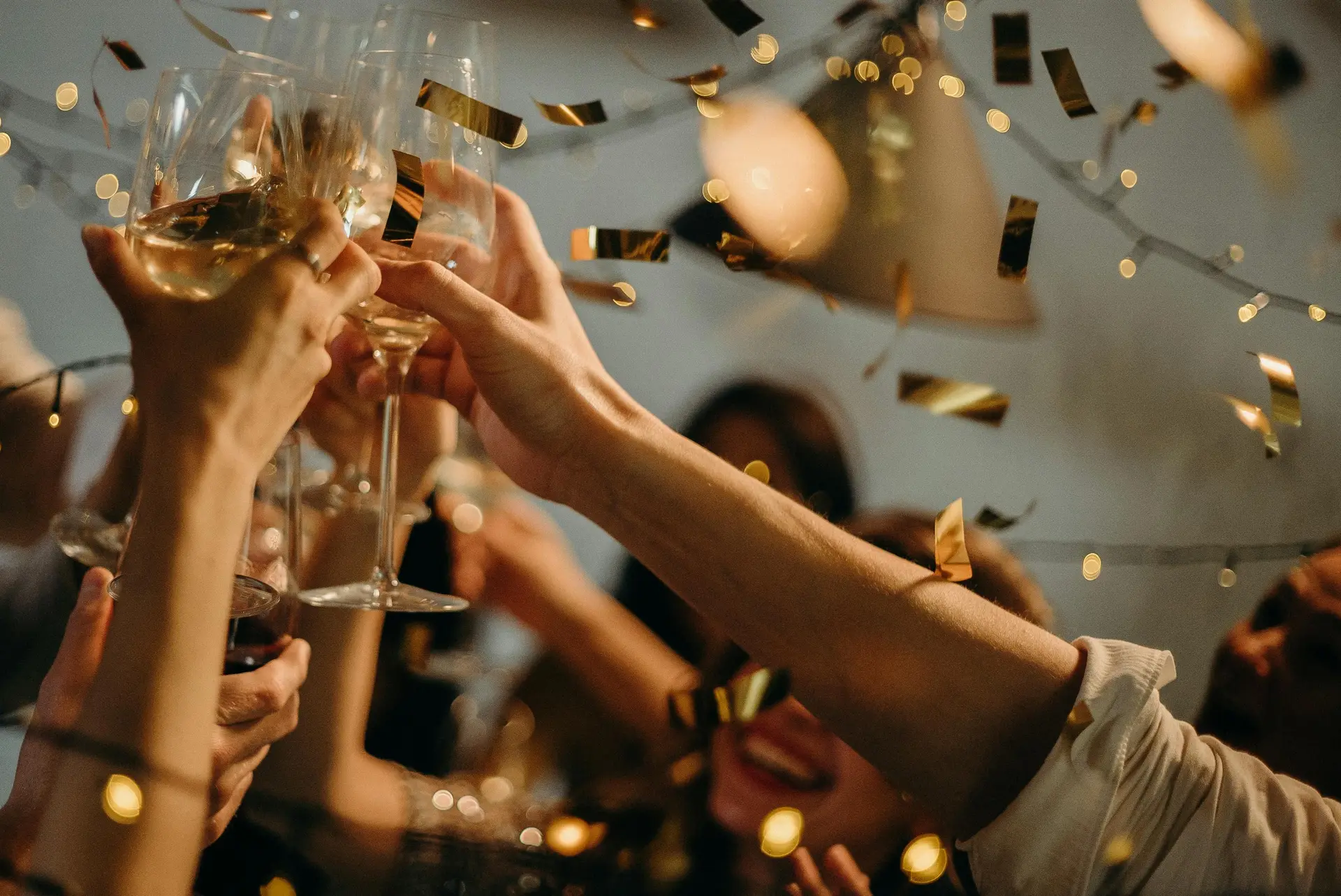 Hands of people clinking drinks with golden confetti papers.