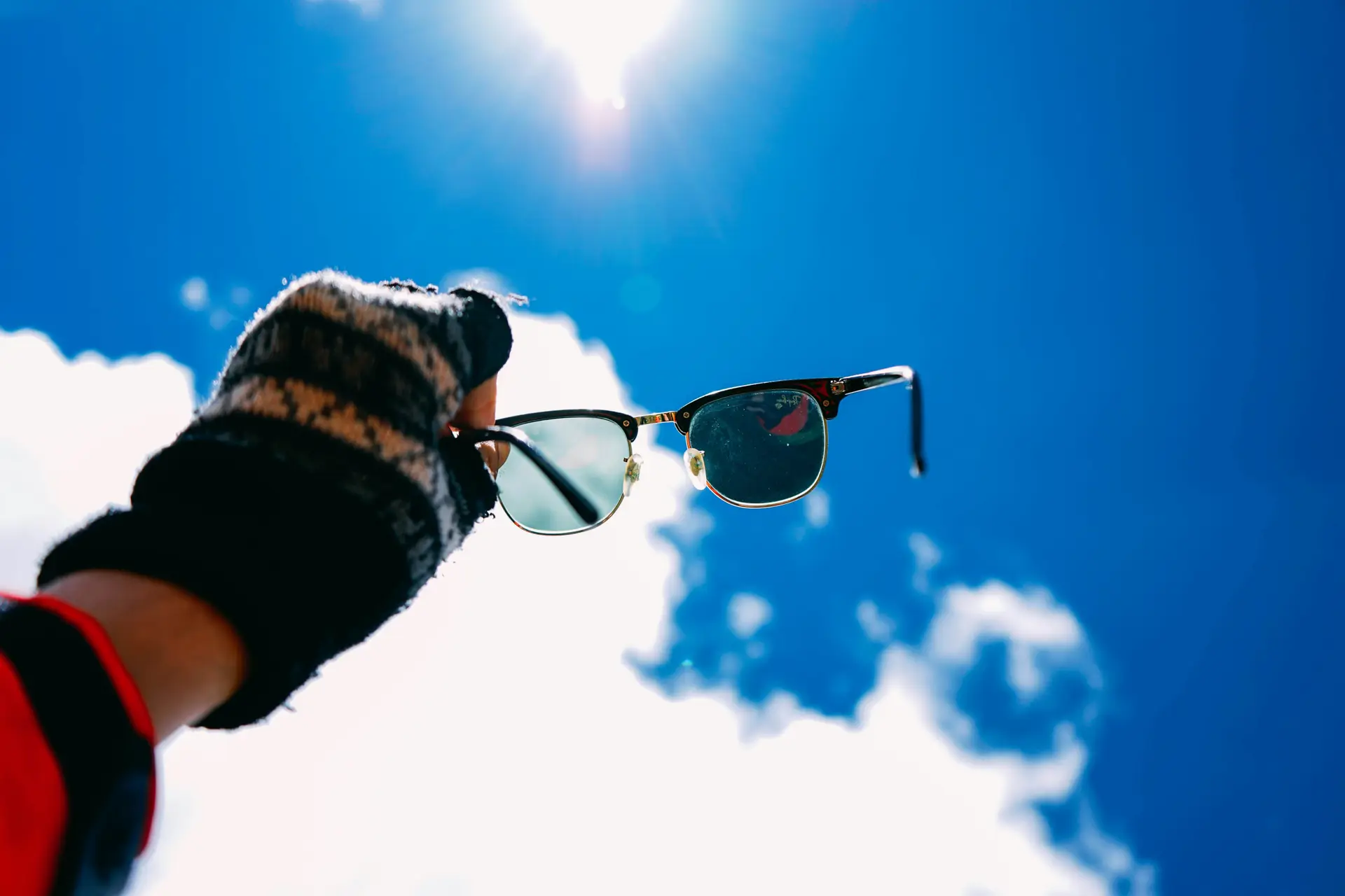 A person holding a pair of sunglass towards the sky.