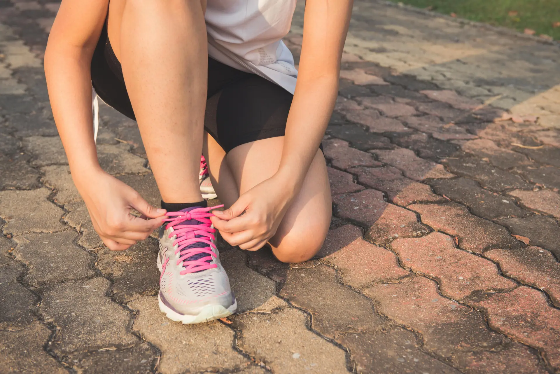 Woman lacing up her gray and pink Nike low-top athletic shoe.