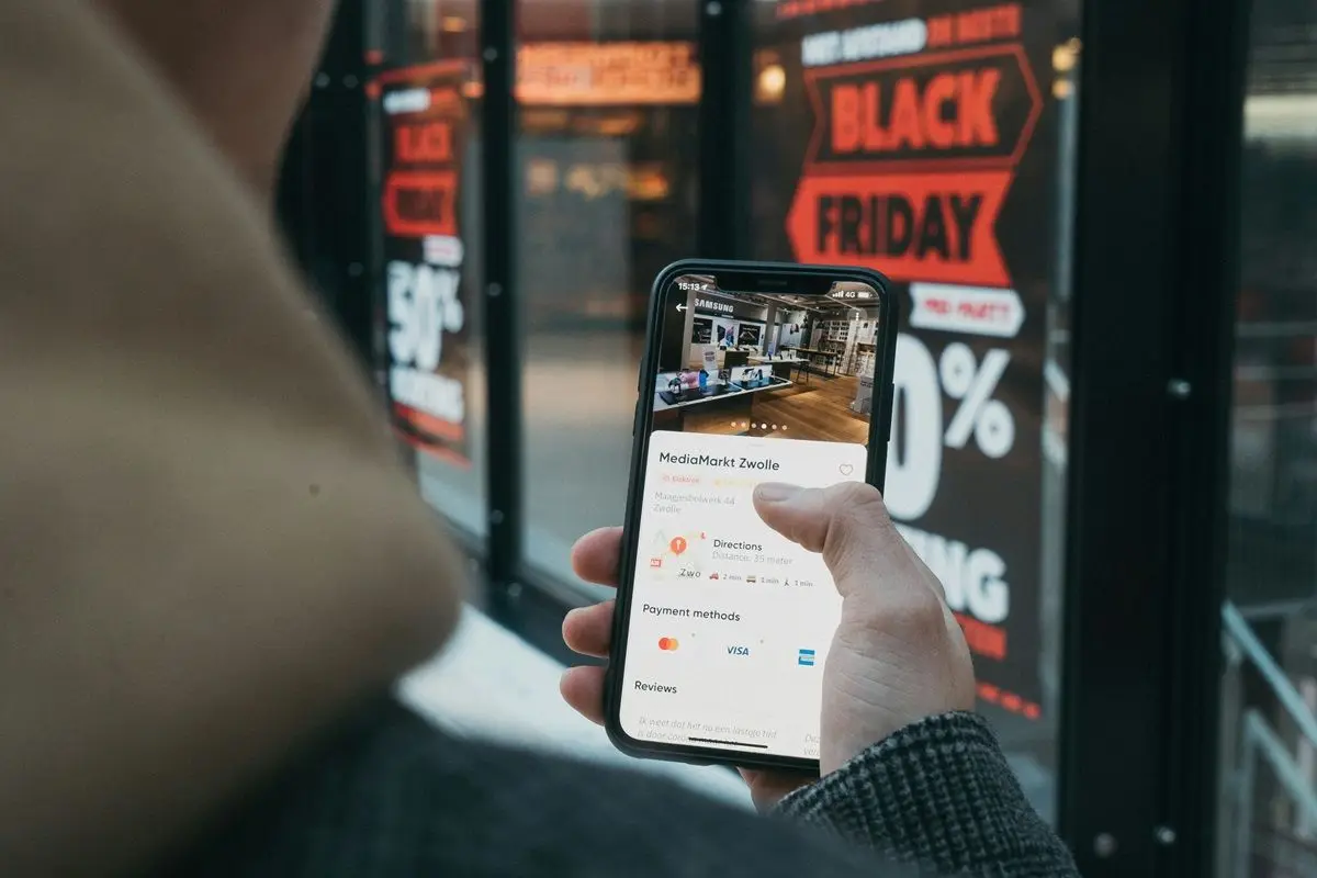A person holding their smartphone in front of a Black Friday sales sign.
